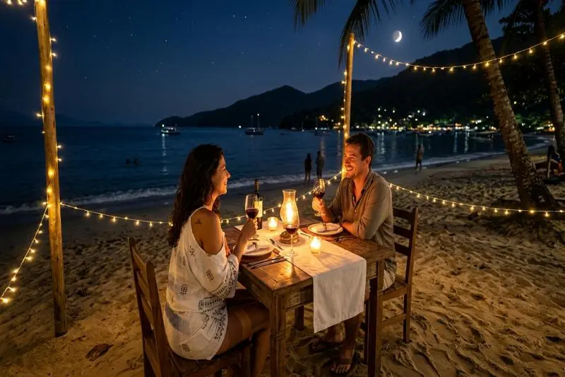 Mesas de madeira com velas na areia da praia durante a noite na Vila do Abraão, Ilha Grande.