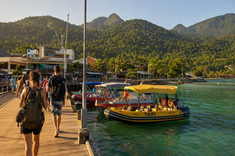 Vista da Vila do Abraão em Ilha Grande, mostrando pousadas rústicas à beira-mar, barcos ancorados e montanhas cobertas pela Mata Atlântica.